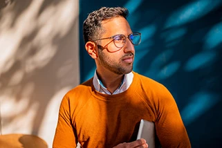 Man with orange jumper holding a laptop